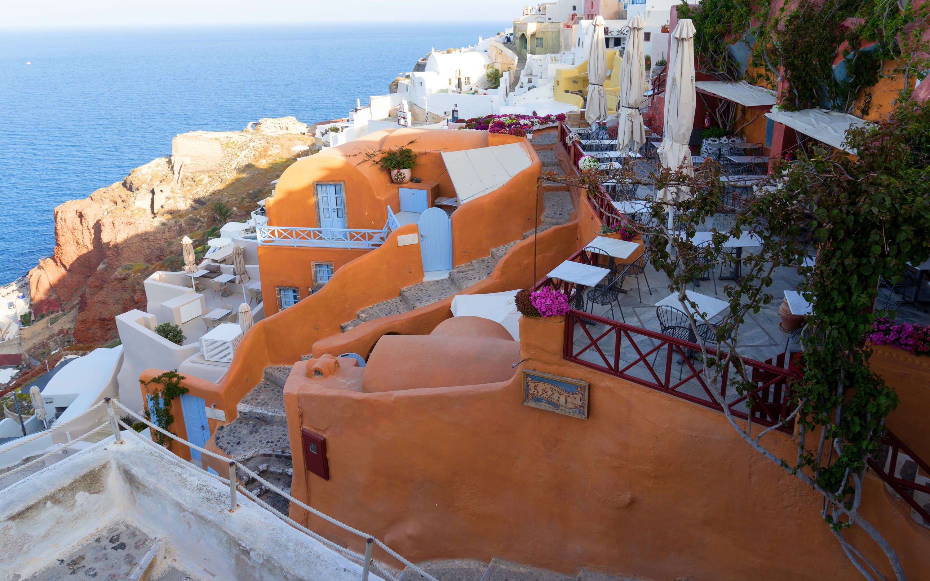             Fototapete Terrasse an der Küste Santorinis – Premium Glattvlies
        